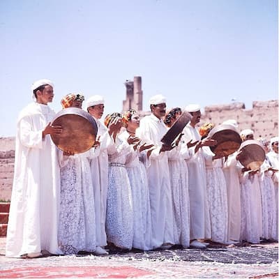 Image représentant un groupe d'Amazighe dansant et jouant des instruments de musique, vêtus d'habits traditionnels. 